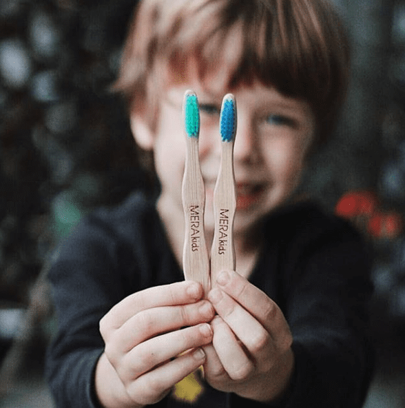 niño que sostiene en su mano 2 cepillos de dientes con cerdas de color verdes y azules